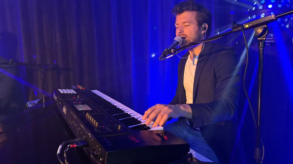 De zanger achter zijn keyboard in blauw podiumlicht tijdens een optreden